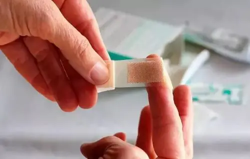 一只手正在为手指贴上创可贴的特写，用于演示创口贴正确使用方法。